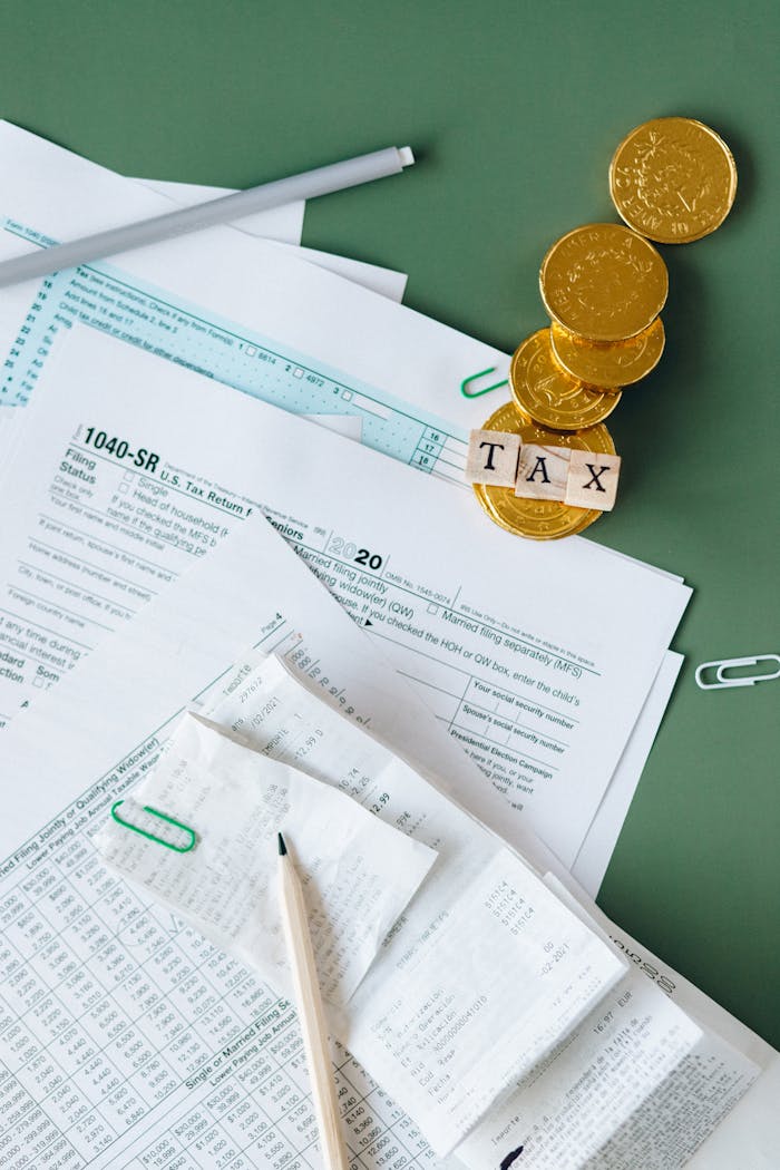 about-us Tax documents and gold coins on a green desk symbolizing financial planning and savings.